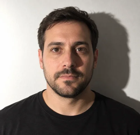 AI-generated photo of a man with a beard in a black T-shirt in front of a white wall, with a dark shadow of his head on the wall to the right