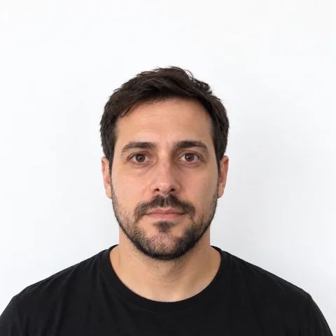 AI-generated photo of a man with short dark hair and a beard in a black T-shirt, facing the camera in front of a plain white wall