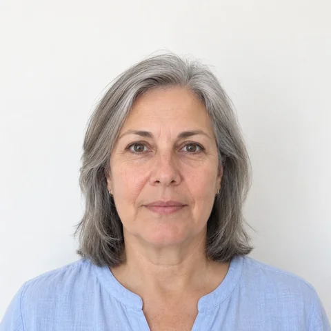 AI-generated photo of a woman with shoulder-length gray hair in a light blue blouse, facing the camera in front of a plain white wall