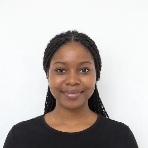 AI-generated photo of a woman with long braids in a black top, with a small closed-mouth smile, in front of a plain white wall